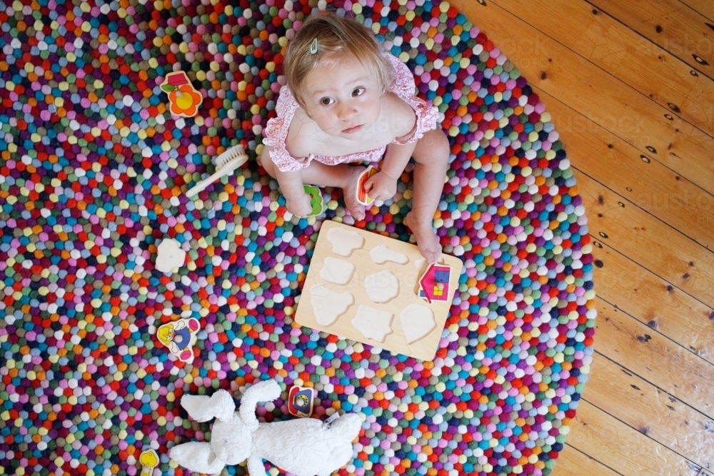 Baby girl on rug with toys looking up - Australian Stock Image