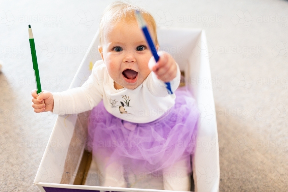 Image of Baby girl sitting in box drawing with crayon textas at home ...