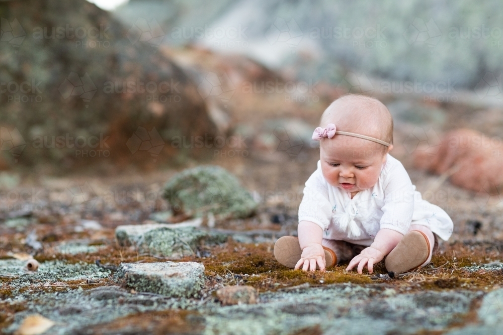 Baby girl sitting on ground touching moss - Australian Stock Image