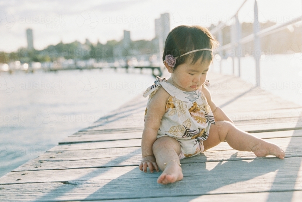 Baby girl sitting on wharf. - Australian Stock Image