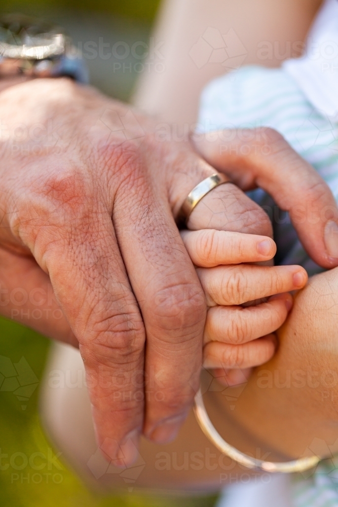 Baby hand wrapped around parents finger wearing wedding band ring - family concept - Australian Stock Image