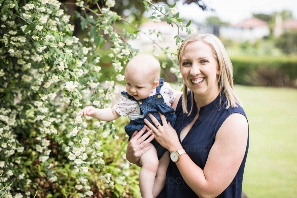 Baby in mother's arms playing with white flowers - Australian Stock Image