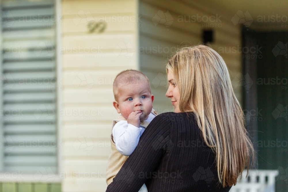 Baby in mums arms looking over his mother's shoulder outside home - Australian Stock Image
