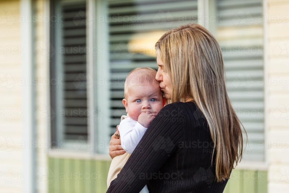 Baby in mums arms looking over his mother's shoulder outside home - Australian Stock Image