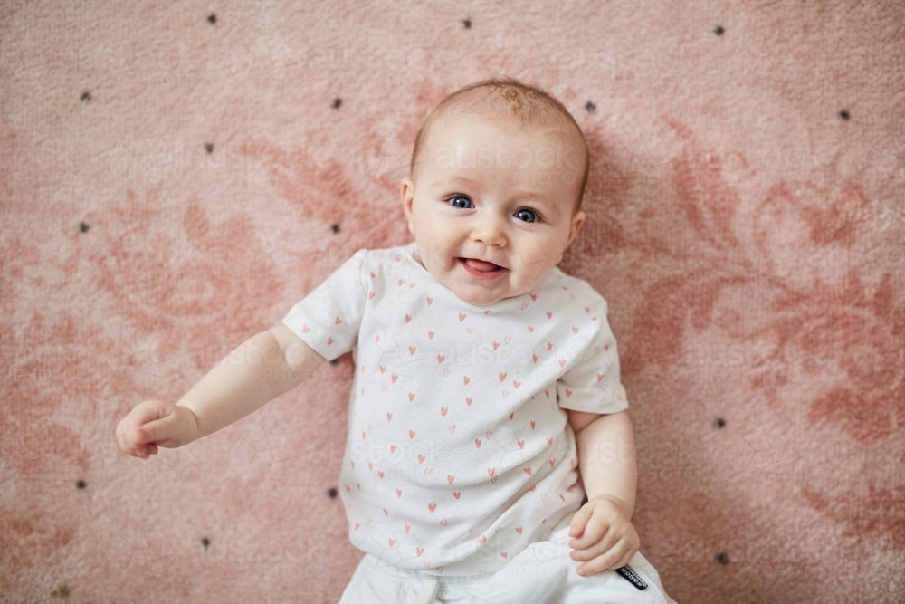Image of Baby laying on pink rug smiling - Austockphoto