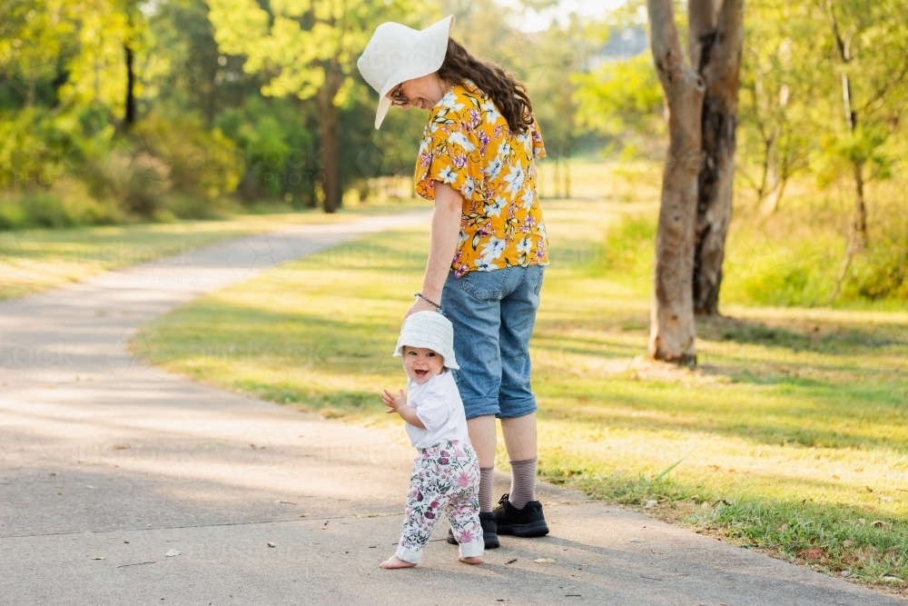 Image of Baby looking back as she walks with parent down footpath ...