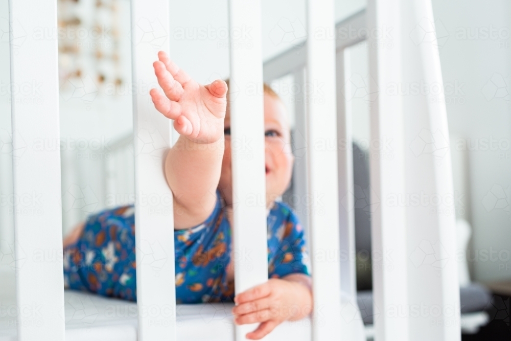 Image of Baby on tummy in cot holding onto white cot bars in bedroom