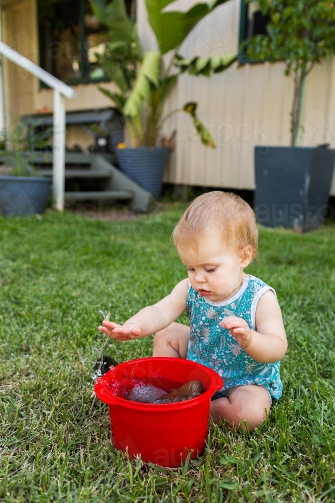 baby playing in backyard with container of rocks and water - Australian Stock Image