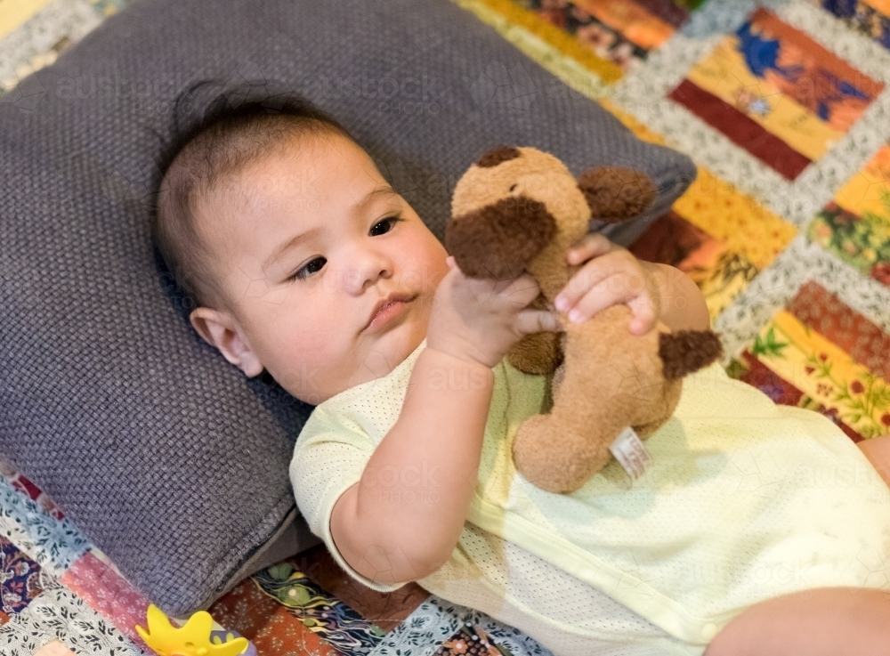 Baby playtime on a mat with puppy plush toy - Australian Stock Image