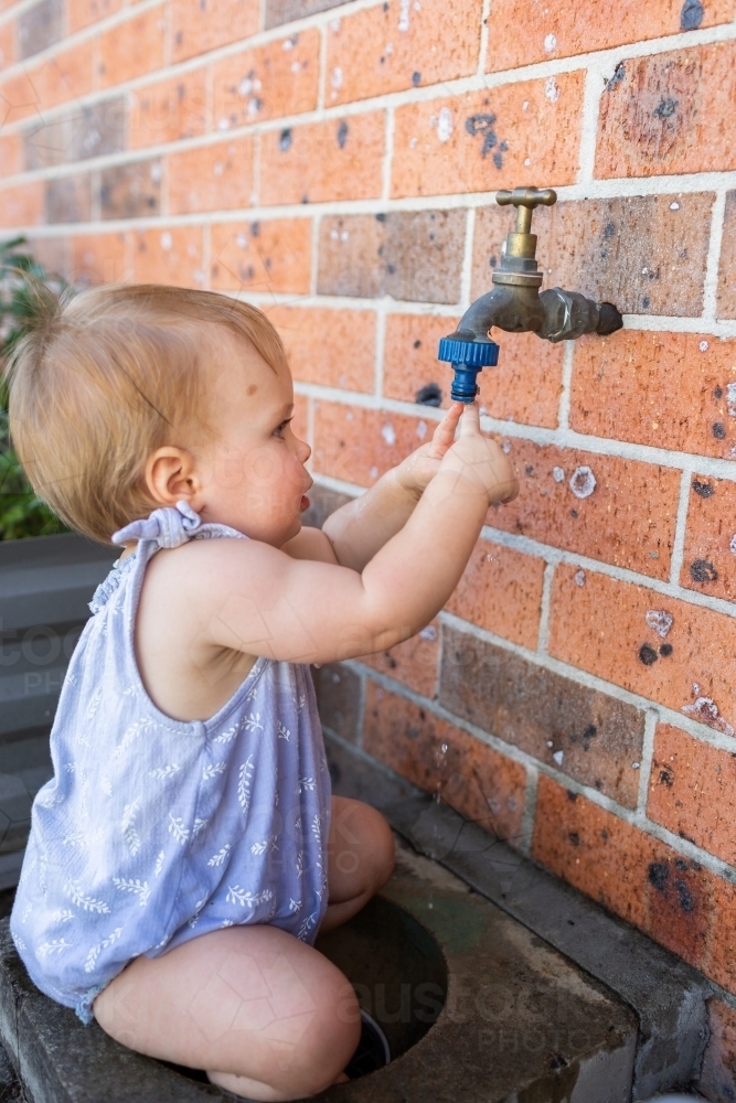 baby putting fingers in tap in backyard, messy water play - Australian Stock Image