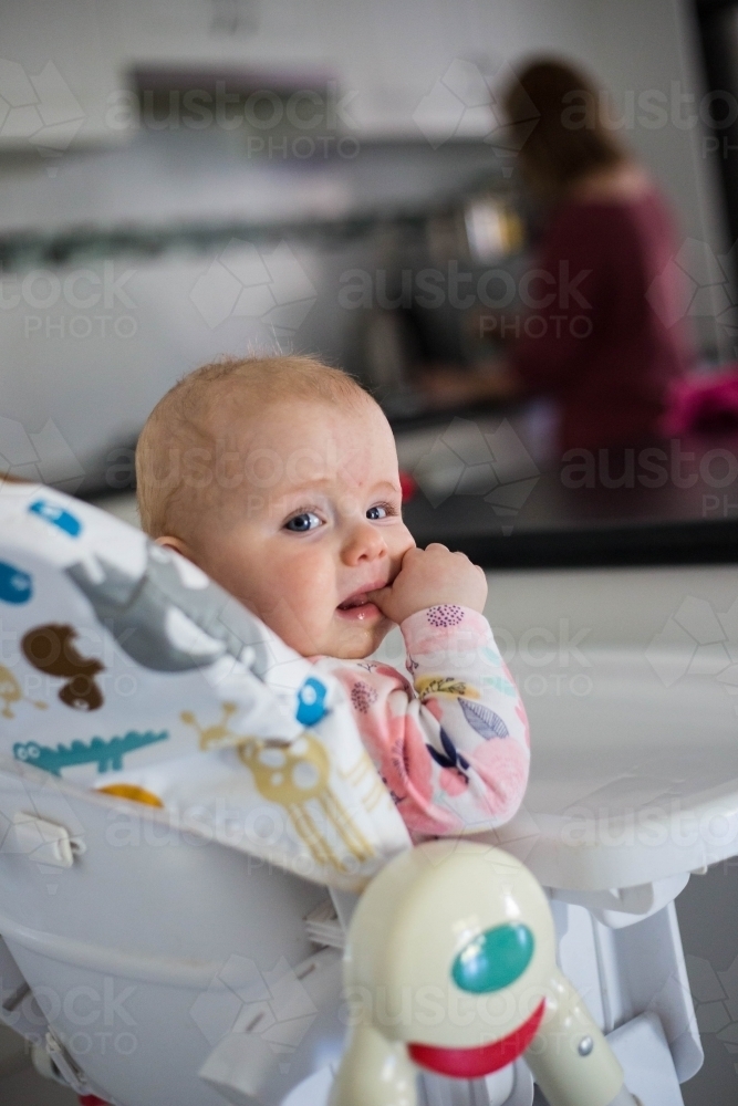 Baby sitting in high chair with thumb in mouth - Australian Stock Image