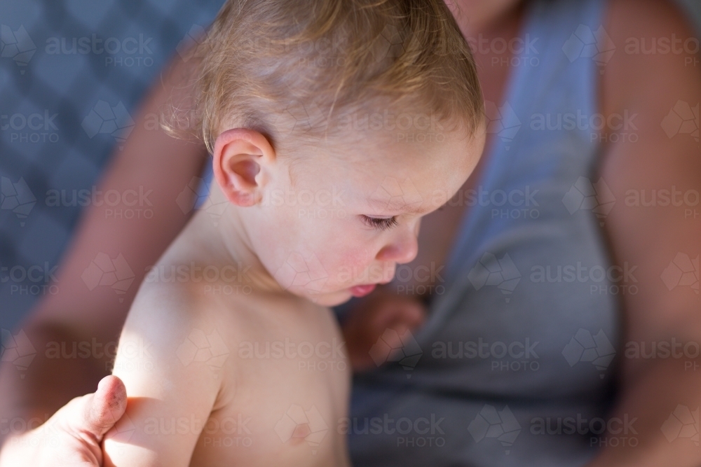 Baby sitting on mother's lap, looking away - Australian Stock Image