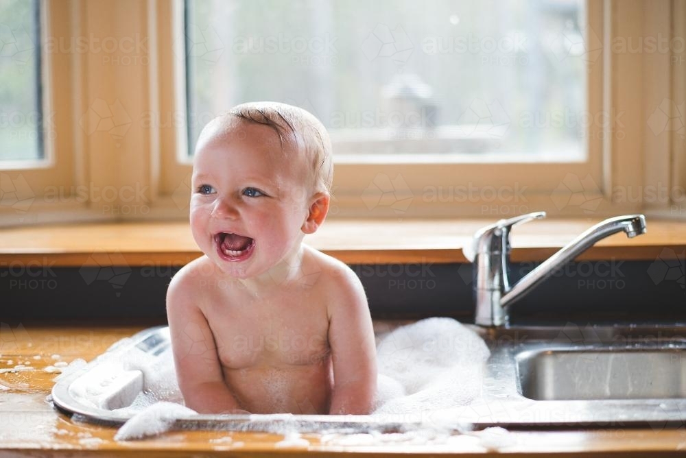 Image Of Baby Smiling And Having A Bath In Kitchen Sink