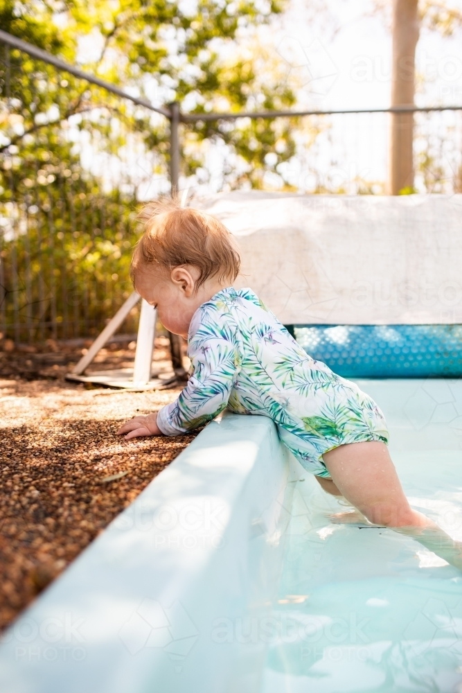 Image of Baby standing on step in backyard swimming pool unsupervised Austockphoto