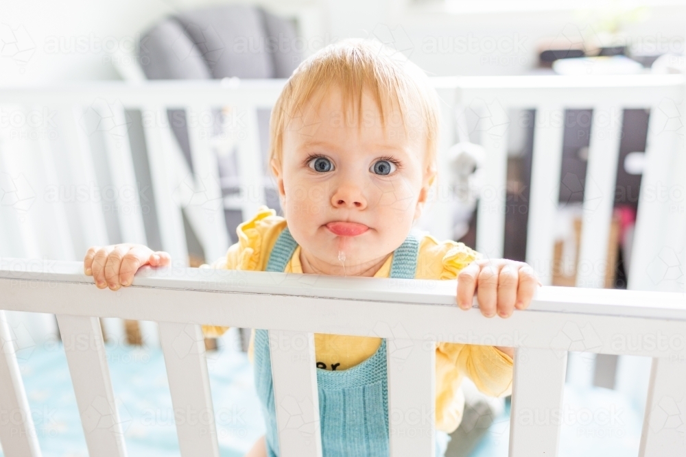 baby with wide eyes pulling silly face with lip in cot - Australian Stock Image