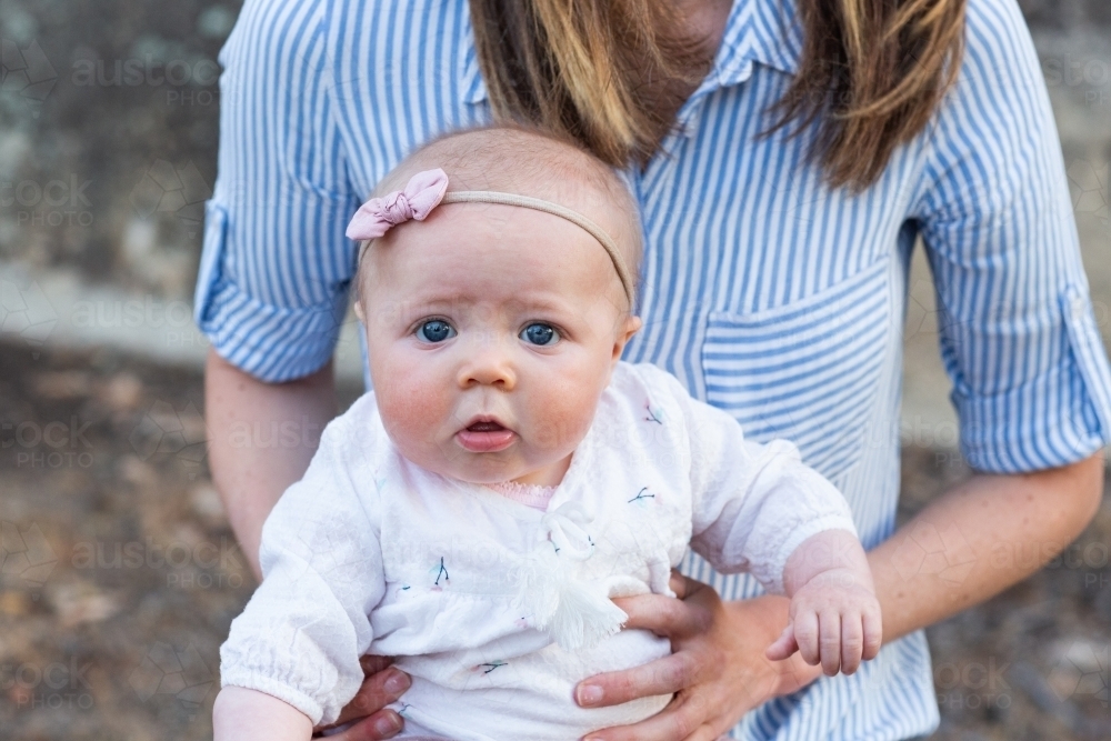 Baby with worried face sitting on mother's lap - Australian Stock Image