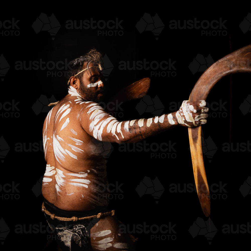 Back of Aboriginal male holding up boomerang to the side - Australian Stock Image