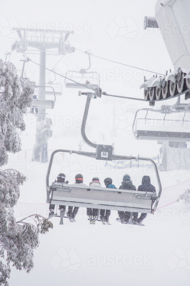 Back of chairlift with 6 skiers going up mountain in the snow - Australian Stock Image