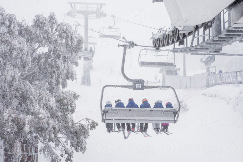 Back of chairlift with 6 skiers going up mountain in the snow - Australian Stock Image