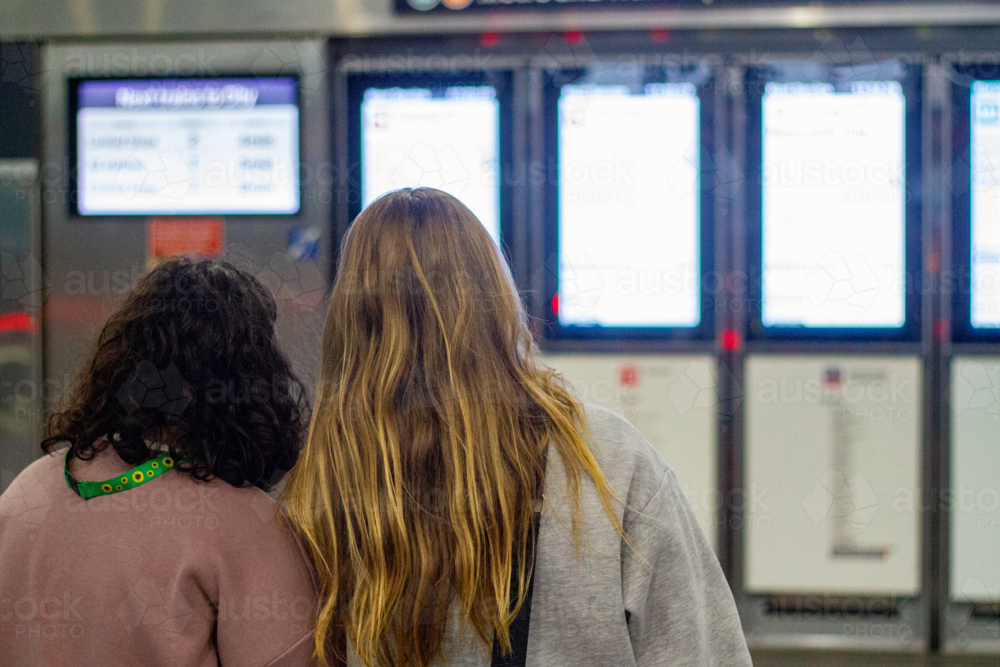 Back profile of two young women standing facing a row of digital information screens - Australian Stock Image