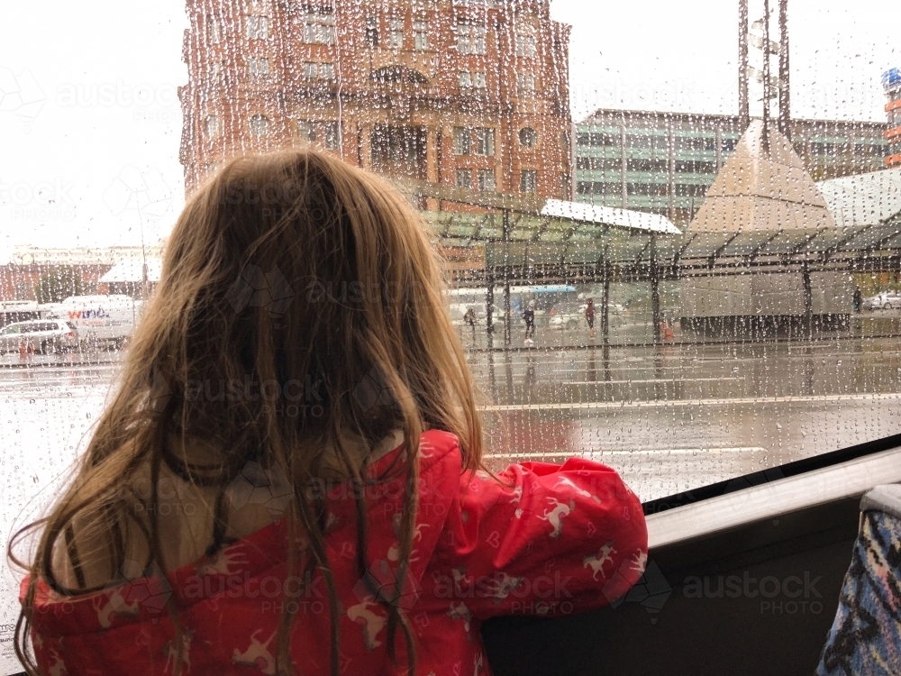 Back shot of a girl looking to the tall building with water droplets on train window glass - Australian Stock Image