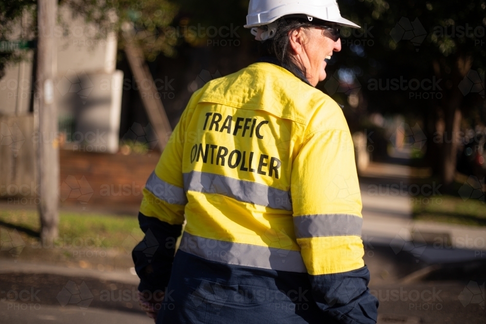 Back shot of a smiling traffic controller woman wearing white helmet and yellow jacket - Australian Stock Image