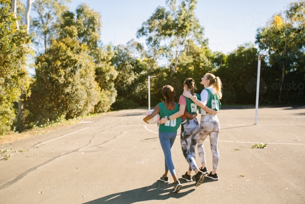 back shot of three young female athletes walking in a field on a sunny day with trees and clear sky - Australian Stock Image