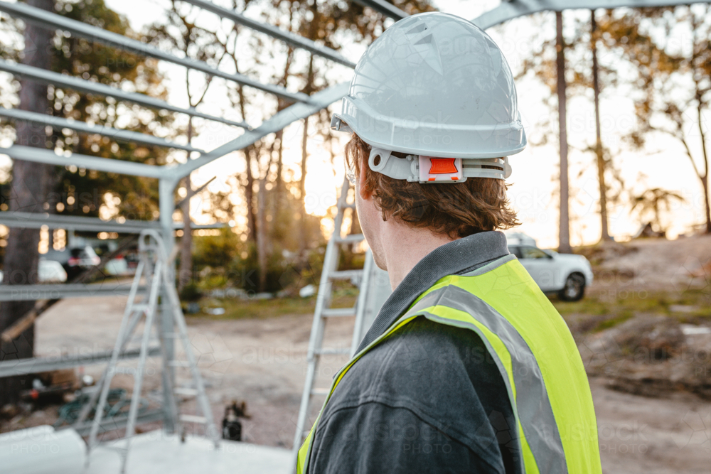 Back view of a man wearing a hard hat on the construction site looking away - Australian Stock Image
