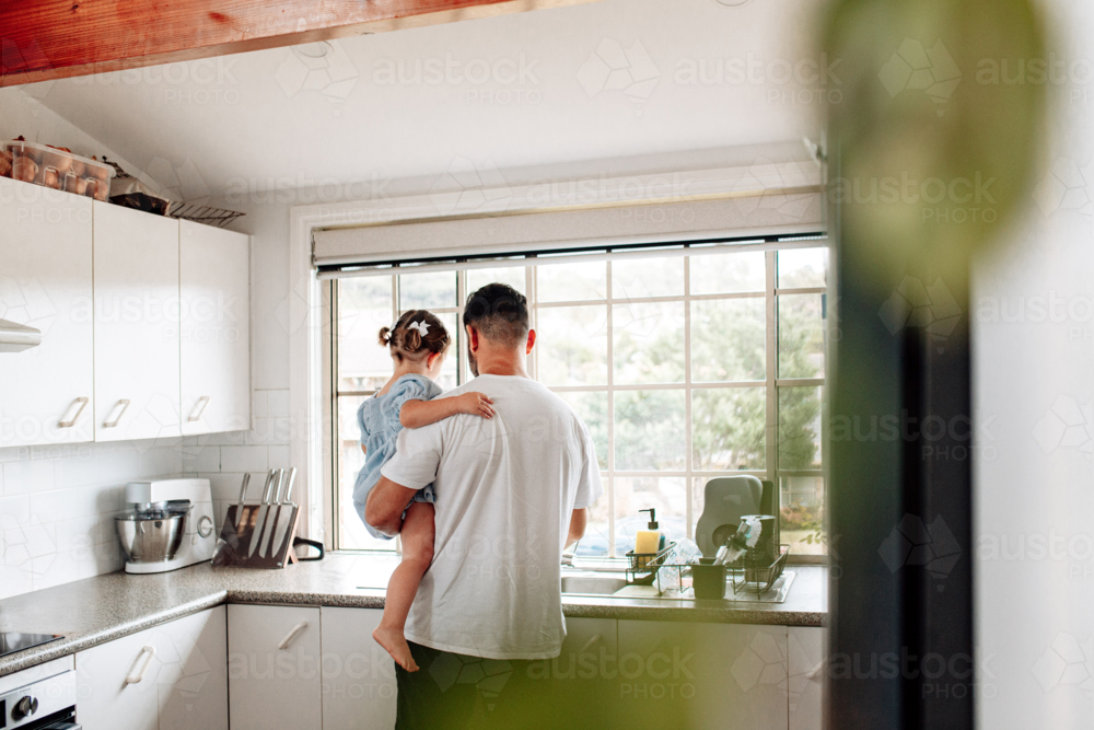 Back view of father carrying toddler daughter in the kitchen. - Australian Stock Image