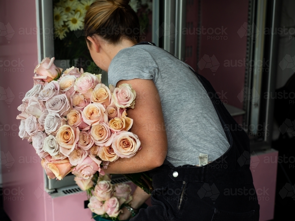 Back view of female florist with a large bunch of beautiful pastel coloured roses - Australian Stock Image