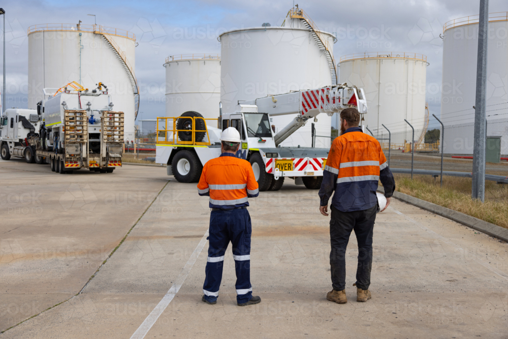 Back view of male workers standing in front of the cherry picker truck in the worksite. - Australian Stock Image