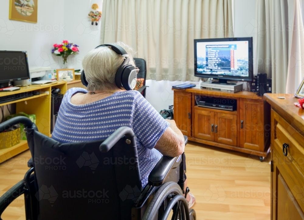 Back view of old grey haired woman in wheelchair watching TV - Australian Stock Image