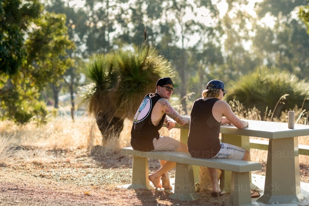 Back view of two guys sitting at a picnic table in a rural setting - Australian Stock Image