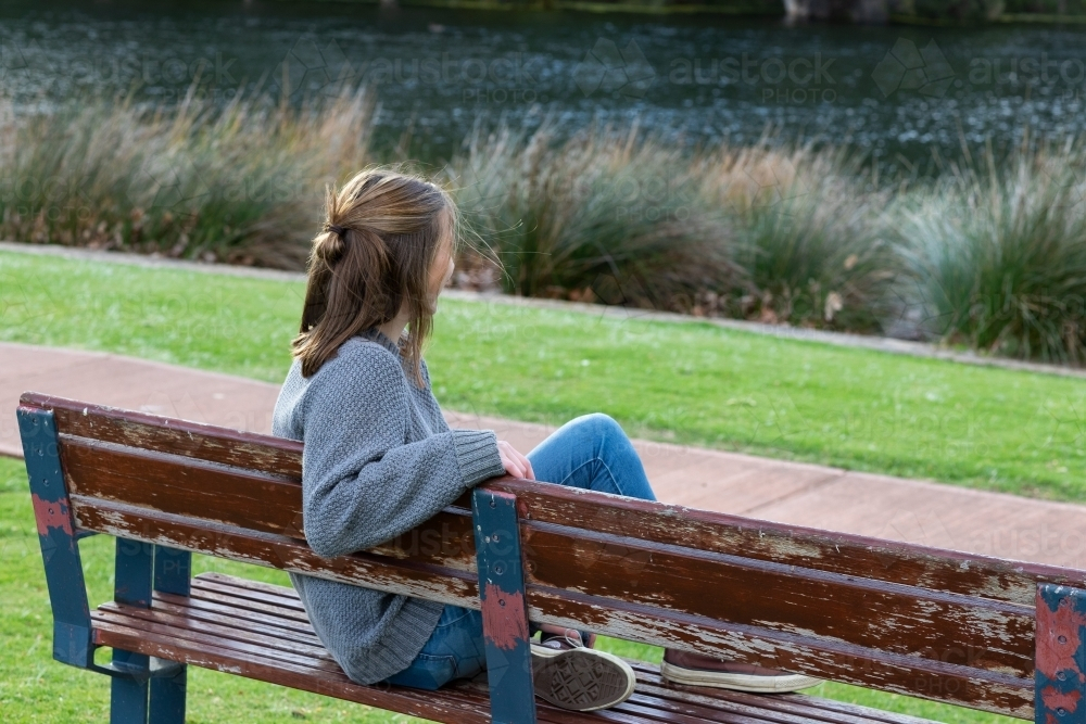 Back view of young woman sitting on park bench - Australian Stock Image