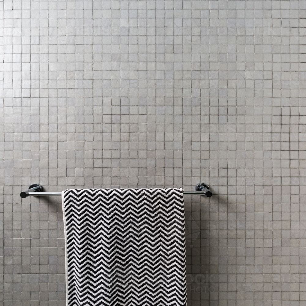 Background of mosaic square wall tiles with chevron towel on chrome towel rail - Australian Stock Image