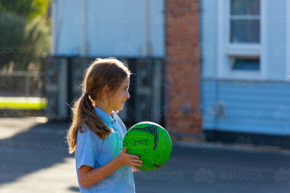 backlit child holding green netball at school - Australian Stock Image