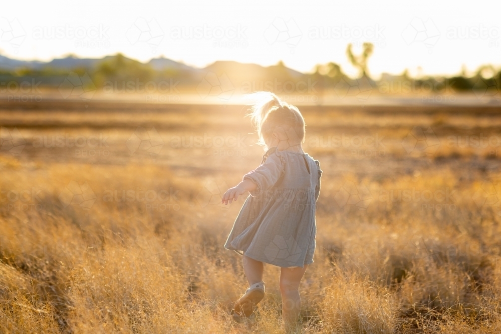 backlit child running through dry grass - Australian Stock Image