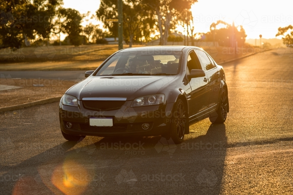 Image of backlit dark coloured car on quiet street in country town with ...