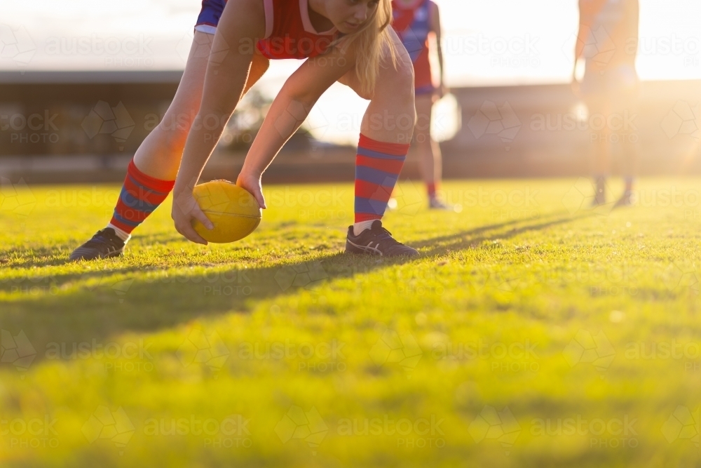 backlit scene with football player picking up football from ground - Australian Stock Image
