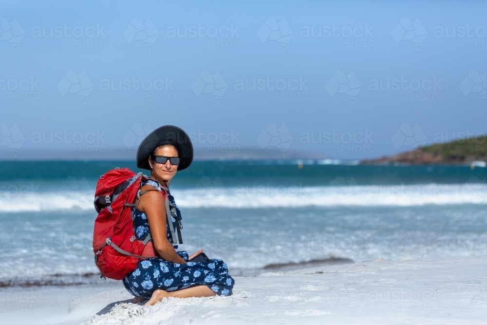 Backpacker with rucksack sitting on white sand beach - Australian Stock Image