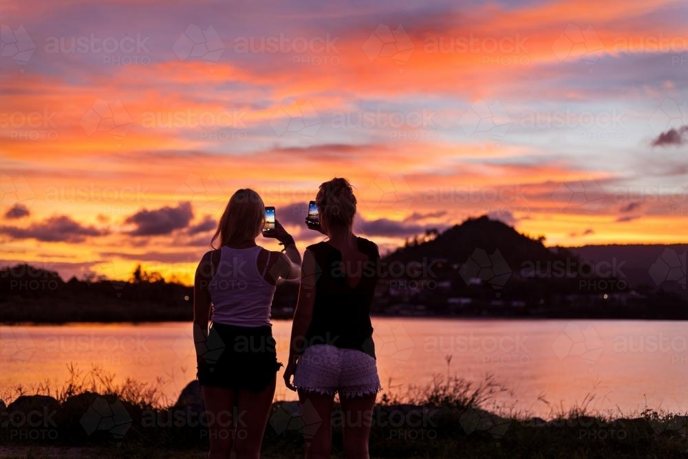 Backpackers photographing a brilliant sunset on their phones. - Australian Stock Image