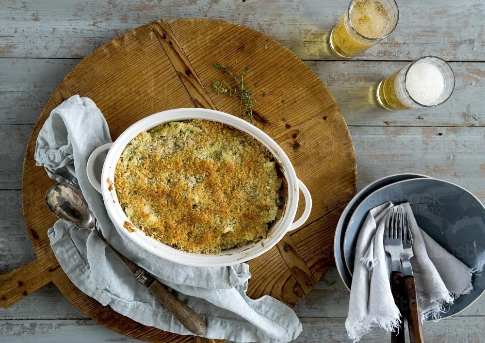 Baked dish on wooden table with beer seen from above - Australian Stock Image