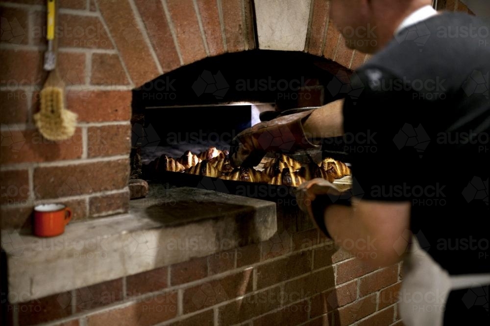 Baker putting croissants into oven - Australian Stock Image