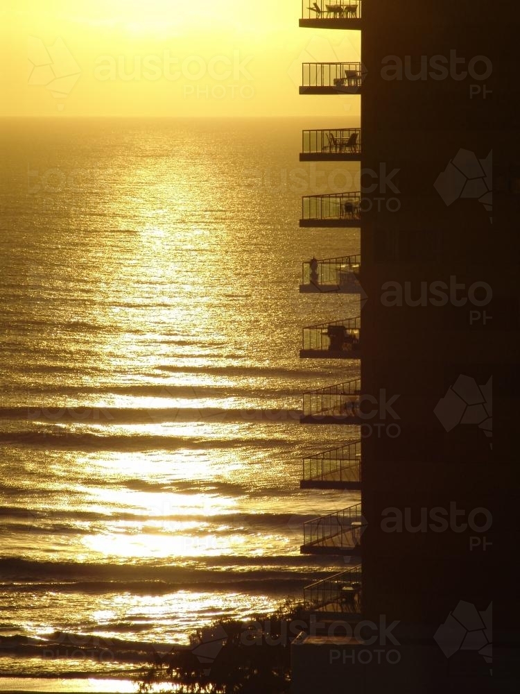 Balconies of a high rise building silhouetted against sunrise across water - Australian Stock Image