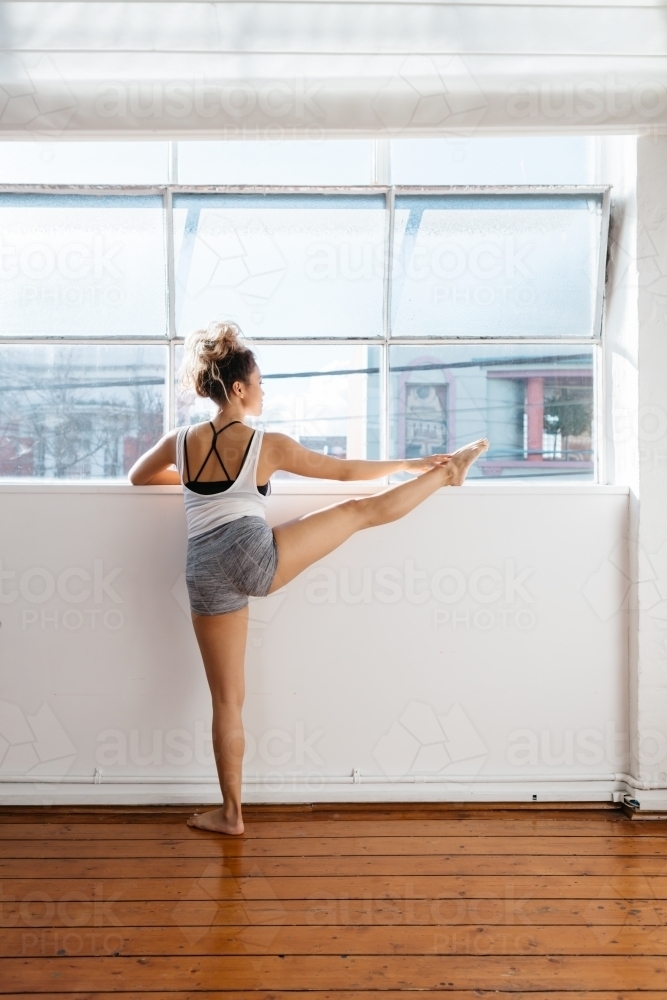Ballet dancer stretching and pointing toes on a ledge in a studio - Australian Stock Image