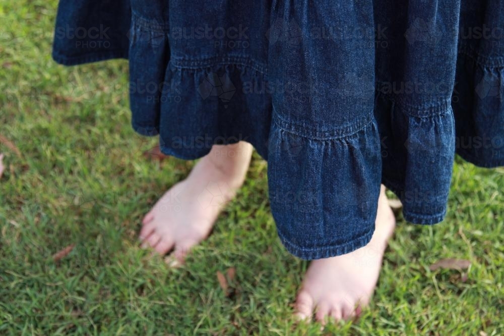 Bare feet of a girl wearing a denim skirt standing in the grass - Australian Stock Image