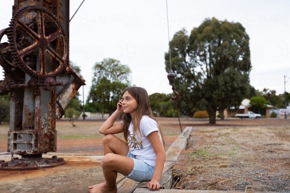 barefoot child by herself near old industrial machinery - Australian Stock Image