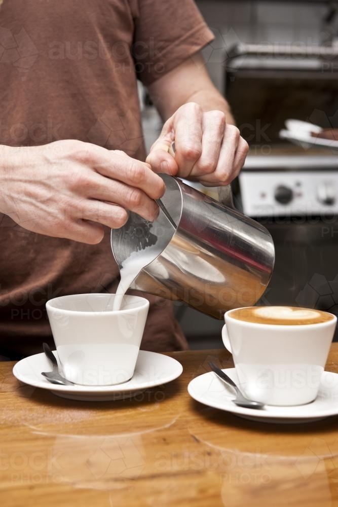 barista pouring milk into ceramic cups - Australian Stock Image