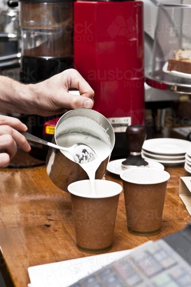 barista pouring milk into takeaway coffee cups - Australian Stock Image