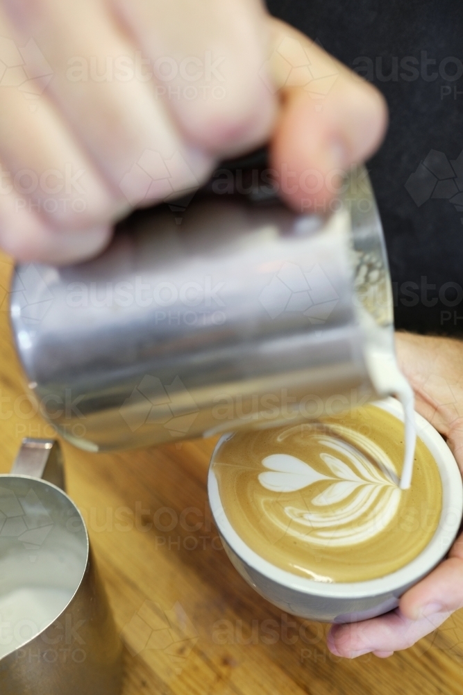 Barista pouring milk to make coffee art - Australian Stock Image